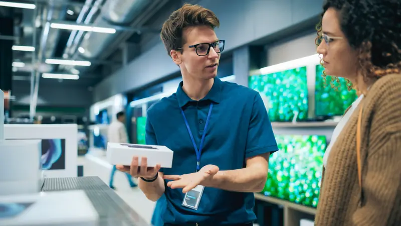 Verkäufer zeigt einer Kundin in einem Elektronikmarkt eine Smartphone-Verpackung